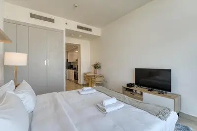 a white bedroom with a large white bed and a flat screen tv at Stylish Studio with Pool, Gym & Tasteful Decor in Dubai