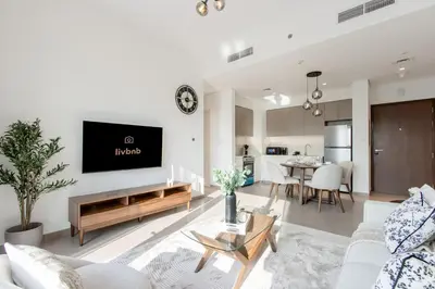 a living room with a couch and a tv on a wall at Livbnb - Stylish 1B in Park Heights Dubai Hills in Dubai