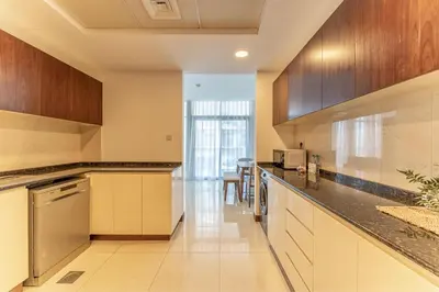 a large kitchen with wooden cabinets and stainless steel appliances at HAVN - 1 Bedroom Apartment in Villa Pera, JVC in Dubai