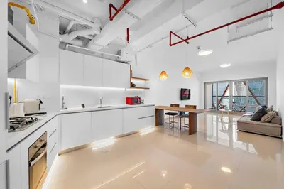 a kitchen with white cabinets and a living room at Chic 1BR APT with Pool, Gym, BBQ, Tennis Court in Dubai