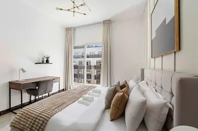 a bedroom with a white bed with a desk and a window at Silkhaus Modern 2BDR in Pantheon Boulevard at JVC in Dubai