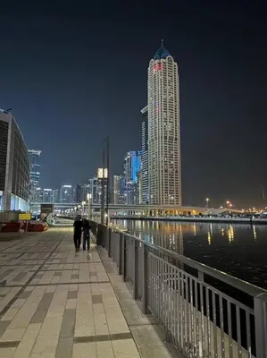 two people walking down a boardwalk near the water at night at Layali - Chic 1BR with Balcony in Business Bay in Dubai