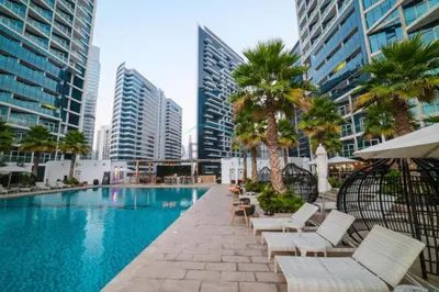 a swimming pool with chairs and palm trees and buildings at Luxury Studio Apartment in Prive By Damac B, Business Bay by Deluxe Holiday Homes in Dubai