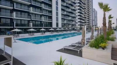 a swimming pool with chairs and umbrellas next to a building at Cozy & Stylish 1br Apt Jvc Pool & Parking in Dubai
