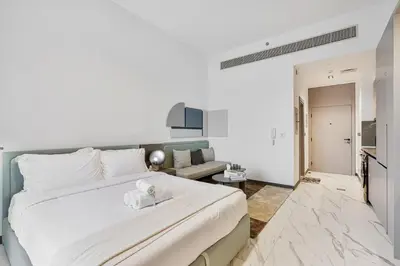 a bedroom with a large white bed and a living room at Lovely Studio in Mag 900, Meydan in Dubai