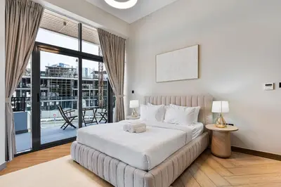 a white bedroom with a bed and a balcony at Modern 2 BR Apartment near Dubai Butterfly Garden in Dubai