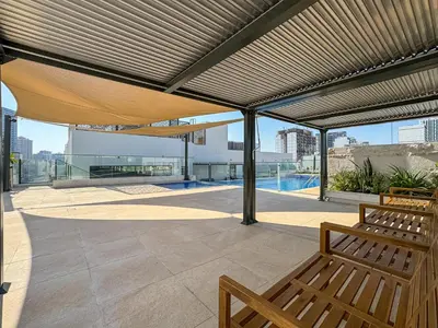 a patio with a wooden bench under awning at Modern Studio with Pool, Gym and BBQ area in Dubai