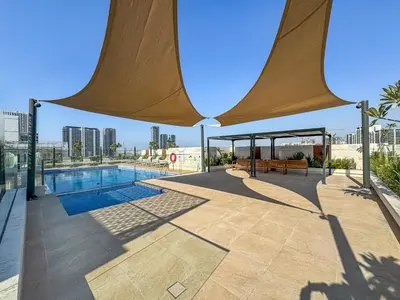 a swimming pool with a large umbrella over it at Modern Studio with Pool, Gym and BBQ area in Dubai