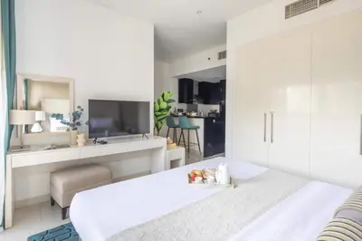 a white bedroom with a bed and a living room at Frank Porter - Damac Cour Jardin in Dubai