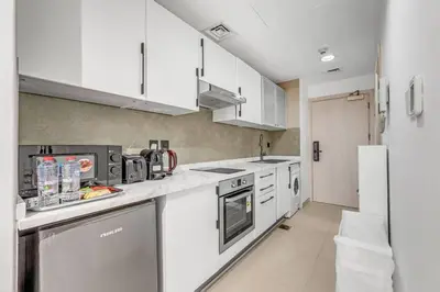 a white kitchen with white cabinets and appliances at Waves - Charming Studio with Lake Views Close to Metro in Dubai
