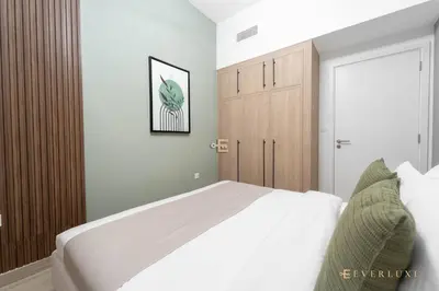a bedroom with a white bed and a wooden cabinet at Chic Liva 1br Family-friendly Great Amenities in Nadd Shubayḩ