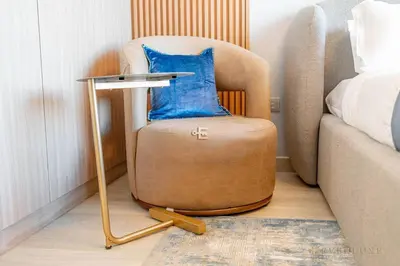 a chair with a blue pillow on it next to a bed at Everluxe Modern Pool View Studio In Al Jaddaf in Dubai