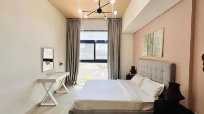 a bedroom with a bed and a desk and a window at Premium 1-Bedroom Perla Apartment in JVC | Infinity Pool & Kids’ Play Area in Abu Dhabi