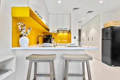 a kitchen with a white counter and two stools at Sleek Brand New Studio in Loci Residence JVC in Dubai