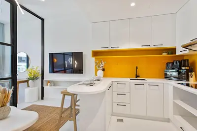 a kitchen with white cabinets and a yellow wall at Sleek Brand New Studio in Loci Residence JVC in Dubai
