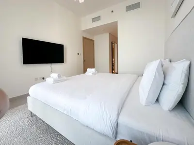 a white bed with white pillows and a flat screen tv at Luxurious 3BR - Pool - Canal View - Kids Play Area in Dubai
