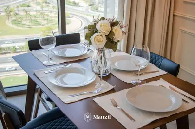 a table with plates and glasses and a vase with flowers at Manzil - 1BR Apartment in Farhad Aziz Residence with Burj View in Dubai