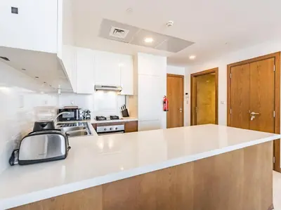 a kitchen with a white counter top and wooden cabinets at Elegant One Bed Apartment - Hameni Tower,JVC in Dubai