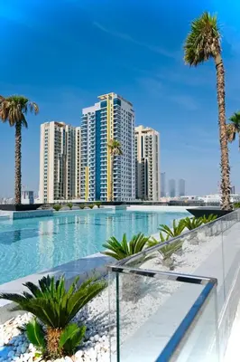 a large swimming pool with palm trees and buildings at Holiday Studio In JVC, Dubai in Dubai
