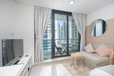 a living room with a couch and a large window at Waves - Cozy Studio with Balcony & Partial Lake Views in Dubai