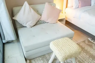 a white couch with pillows and a stool in a room at Waves - Cozy Studio with Balcony & Partial Lake Views in Dubai