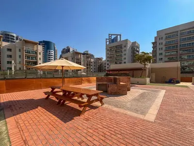 a wooden picnic table with an umbrella on a brick patio at Frank Porter - Al Samar 1 in Dubai