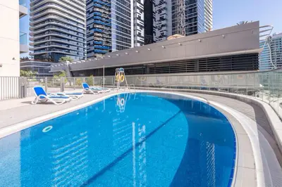 a large blue swimming pool with chairs and buildings at Livbnb - 2B Maid's in Dunya, 5Min Walk to Dubai Mall in Dubai