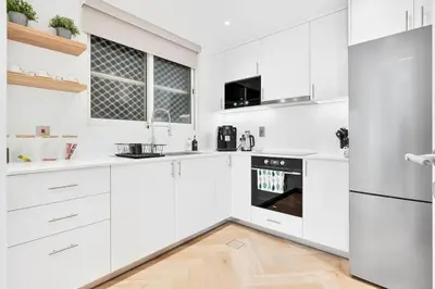 a white kitchen with white appliances and a wooden floor at Urban Oasis 1BR in Armada with Cityscape Views in Dubai