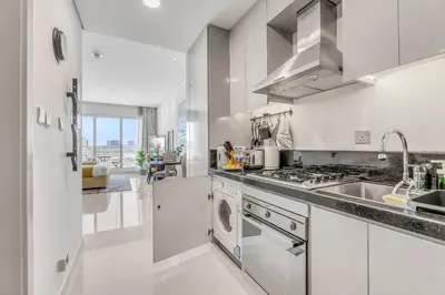 a white kitchen with a sink and a stove at Waves - Stylish Studio with Balcony in Dubai South in Dubai