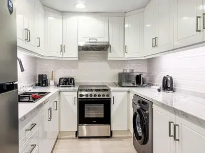 a white kitchen with a stove and a dishwasher at DreamShoma -1B Spacious Apartment with a Lake View in Dubai
