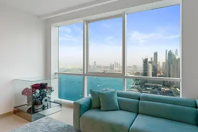 a living room with a blue couch in front of a large window at Ferrari Inspired Modern 3BHK with maids room and Full Sea View in Dubai