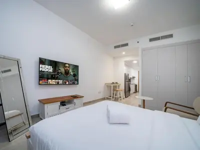 a bedroom with a white bed and a tv on the wall at Bright JVC Studio - Serenity Escape in Dubai