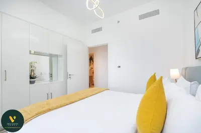 a white bedroom with a white bed and a yellow pillow at Vogue Downtown Views II with Direct Access to Dubai Mall Via a Climate Controlled Bridge, Two Bedroom Apartment with Balcony and Burj Khalifa View in Dubai