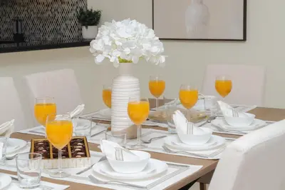 a dining room table with a vase of flowers and glasses of orange juice at Paramount Midtown by Luxe Living in Dubai