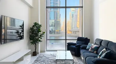 a living room with blue couches and a large window at Canal-View Duplex in Dubai