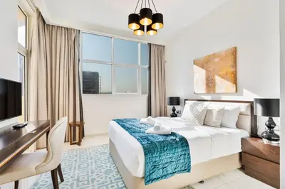 a hotel room with a bed and a desk and a window at Urban Sanctuary Studio with Pool, Gym and Playground in Dubai