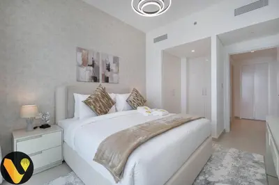a white bedroom with a large white bed with a night stand at Vogue Downtown Views II with Direct Access to Dubai Mall Via a Climate Controlled Bridge, One Bedroom Apartment with Balcony and City View in Dubai
