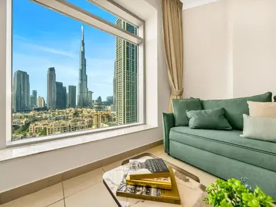 a living room with a green couch and a large window at Royal Vista - Luxury 2BR Apartment at Burj Views Tower A - Downtown in Dubai