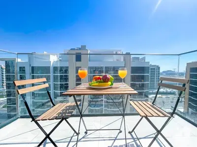 a table with a bowl of fruit and two glasses on a balcony at Elegant Stay in Meydan Balcony & Stunning Views in Dubai