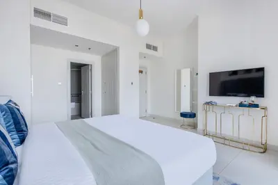 a white bedroom with a large bed and a flat screen tv at Frank Porter - Damac Heights in Dubai