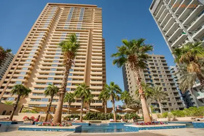 a group of palm trees in front of a tall building at Quirky Studio Apartment in Damac Ghalia in Dubai
