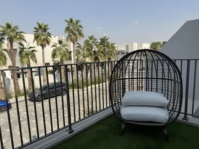 a rattan chair sitting on a balcony with palm trees at New Family Villa with PS5, Garden and Playroom in Dubai