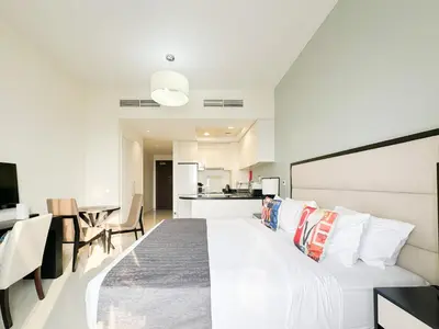 a bedroom with a large white bed and a kitchen at Bespoke Holiday Homes - High floor studio in Tower 108 JVC in Dubai