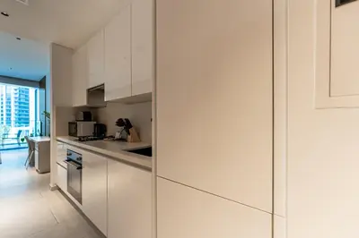 a kitchen with white cabinets and a glass wall at HAVN - New Studio Business Bay, Burj Khalifa View in Dubai