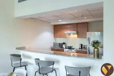 a kitchen with a counter with chairs and a refrigerator at Vogue The Greens Al Dhafrah near Mall of the Emirates, One Bedroom Apartment with Balcony and vibrant community view, Access to all Amenities in Dubai