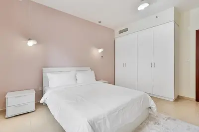 a white bedroom with a white bed and a white cabinet at Savis Home Oceanfront Serenity and Marina Views in Dubai