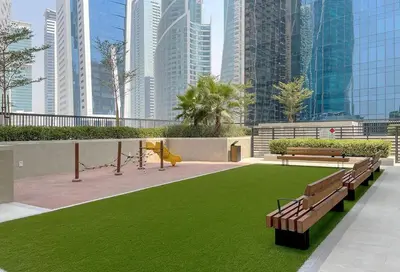 a park with benches and green grass and tall buildings at Luxurious Pool View 1BHK, Zada Tower in Dubai