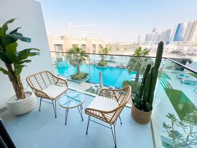 a balcony with two chairs and a table and a pool at Modern Studio in JVC - Pool, Gym & BBQ Access in Dubai