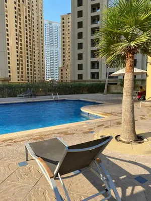 a chair sitting next to a palm tree next to a pool at JBR bed-space in Dubai