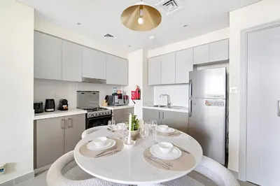 a white kitchen with a table and a refrigerator at 1BR Forte 2, Skyline City View in Dubai